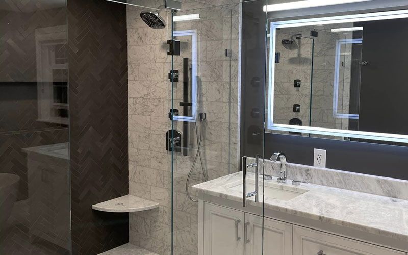 Modern bathroom with a glass-enclosed shower, marble tile walls, illuminated vanity mirror, and white countertop sink.