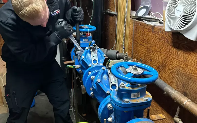 Technician from Armano Plumbing & Heating using a wrench to adjust large blue industrial water valves in a mechanical room.