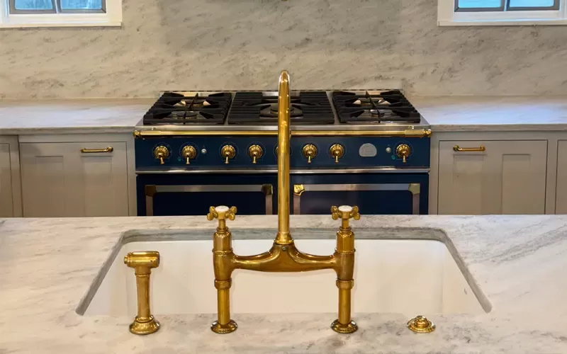 Elegant kitchen with a marble countertop, brass faucet, and a vintage-style blue and brass stove in the background.