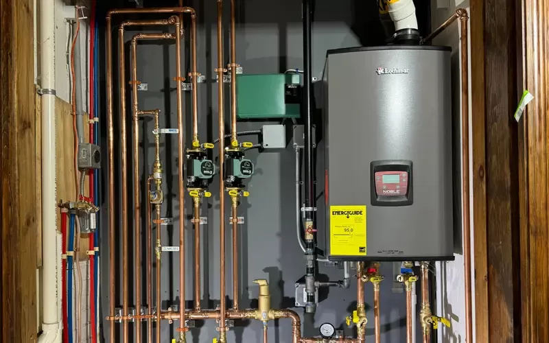 Residential boiler system with a high-efficiency unit, copper piping, valves, and energy efficiency label installed on a gray wall.