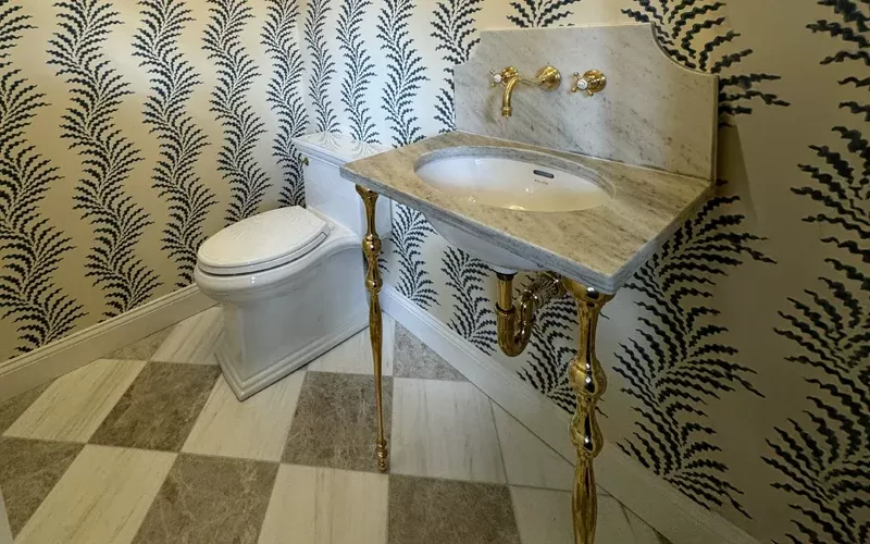 Luxurious bathroom with a marble sink on gold legs, matching gold faucet, patterned wallpaper, and a white toilet on a checkered marble floor.